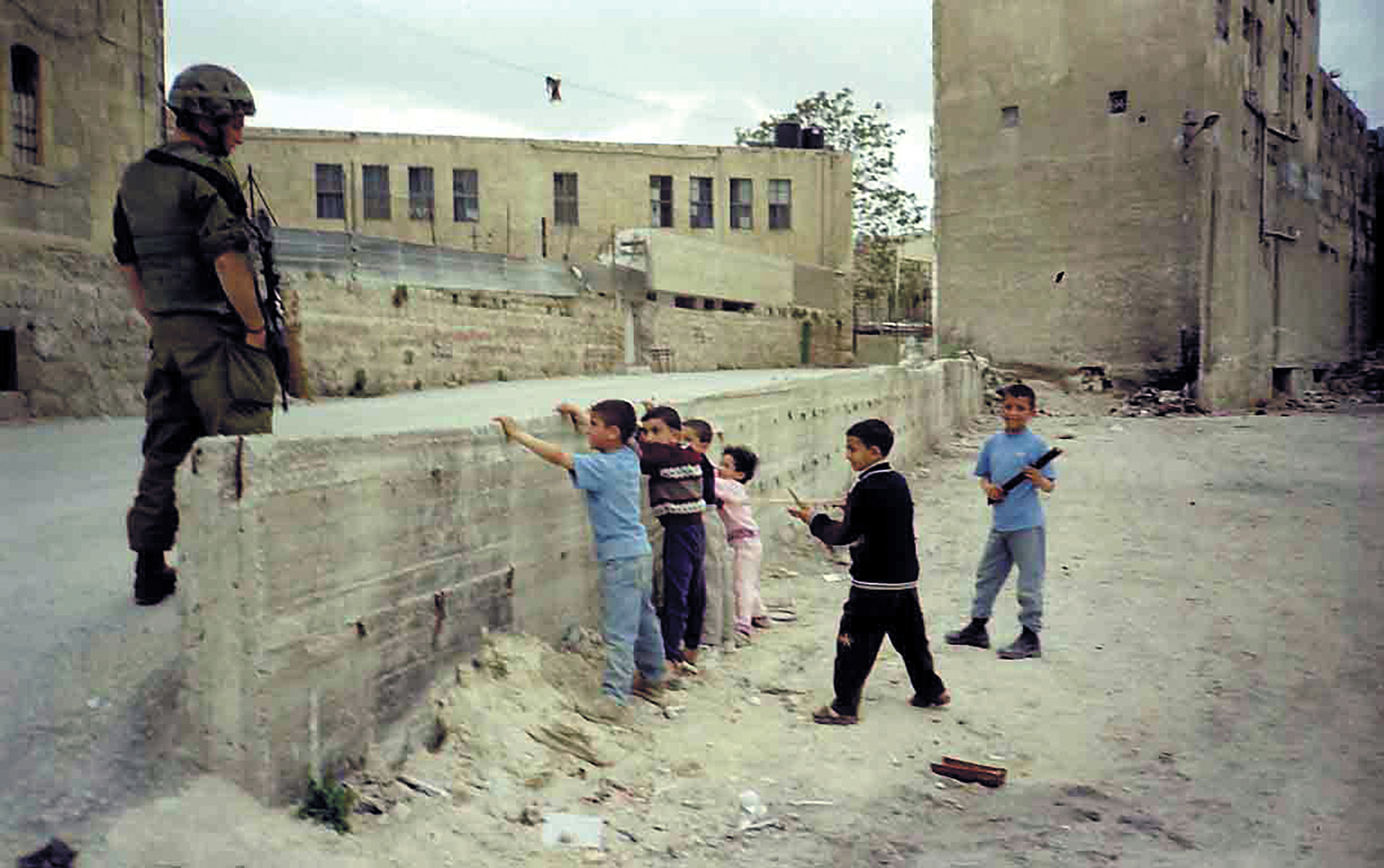 Children playing at soldiers watched by a soldier